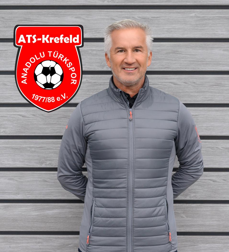 Mann in grauer Jacke steht vor einer grauen Wand, neben dem Logo von ATS Krefeld Anadolu T&uuml;rksport.