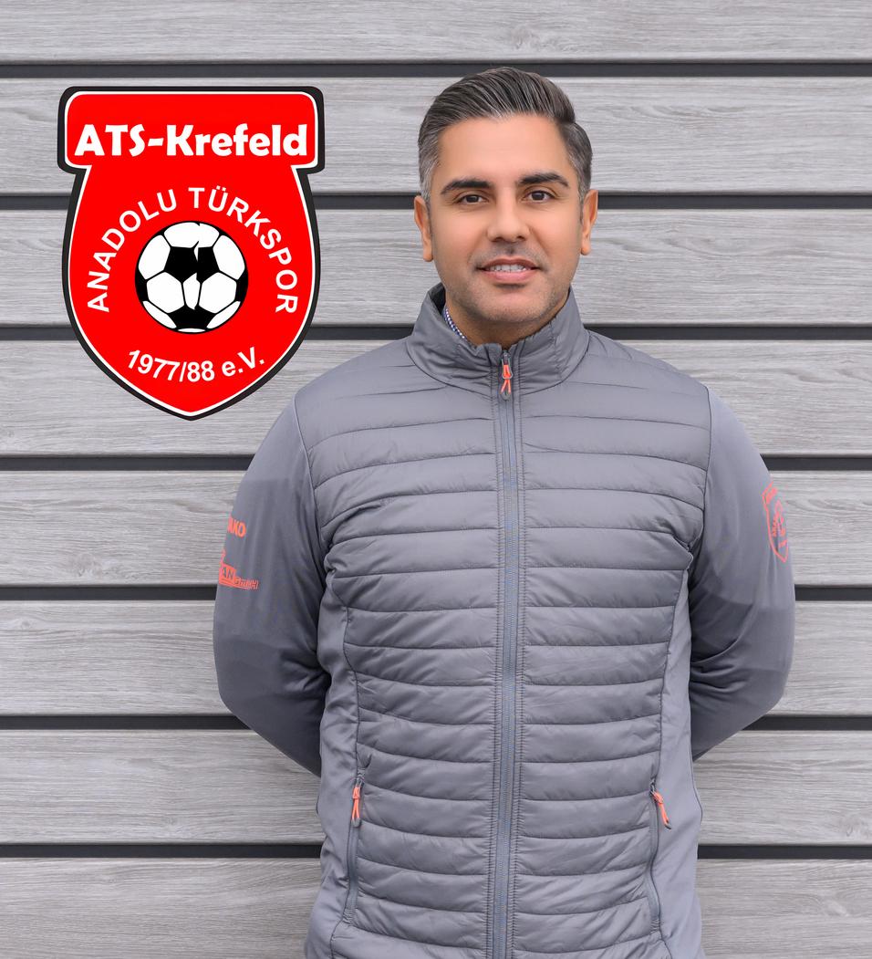 Mann in grauer Jacke steht vor einer Holzwand, neben dem Logo von ATS Krefeld und Anadolu T&uuml;rkspor.