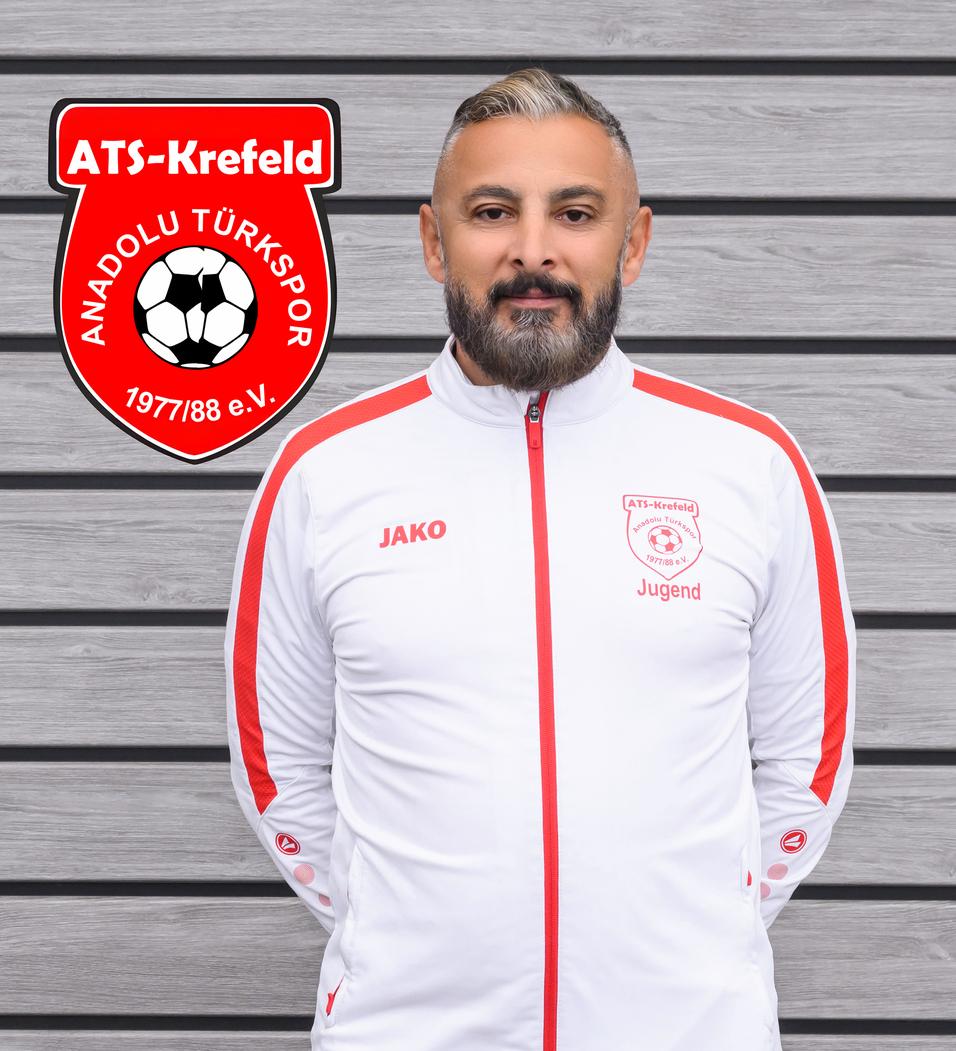 Mann in Sportjacke mit Vereinslogo von ATS Krefeld vor Holzpaneelen im Hintergrund.