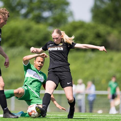 Zwei Fu&szlig;ballspielerinnen im Wettkampf um den Ball, eine Spielerin liegt auf dem Boden, die andere ist in einer aktiven Position.